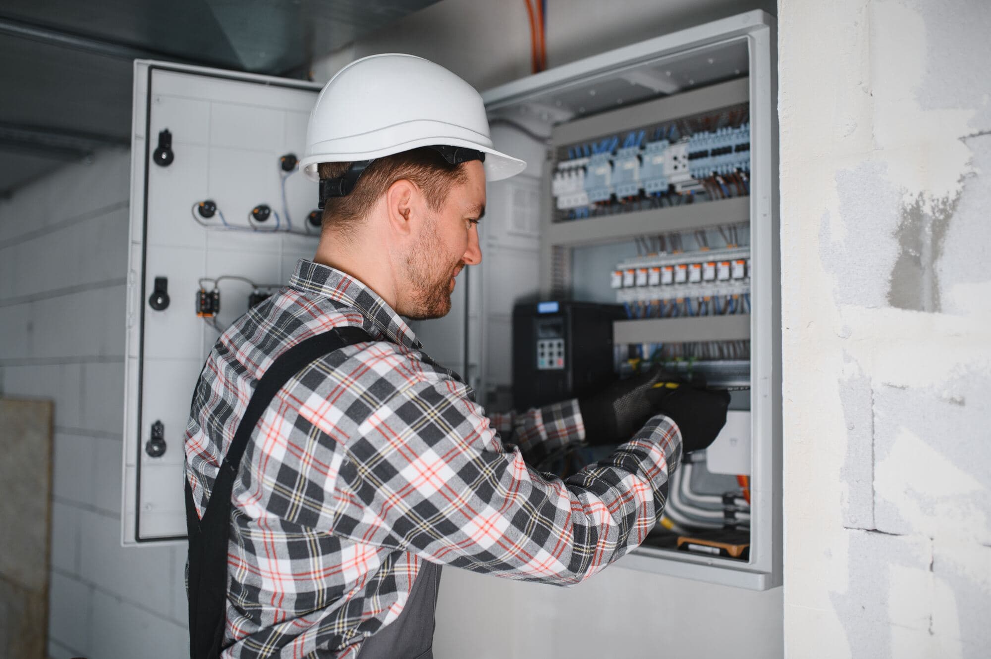 Elektriker i rutig skjorta arbetar i ett större elskåp i en byggnad under ombyggnad